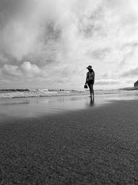 Rear view of woman walking on beach against sky