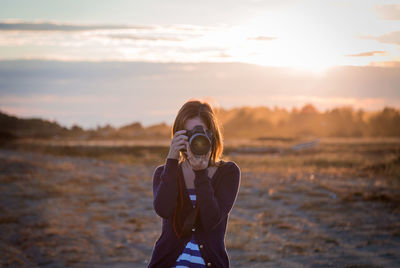 Portrait of woman photographing against sky during sunset
