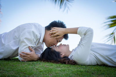 Young couple lying on field against sky