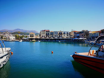 Sailboats moored on canal by buildings against clear blue sky