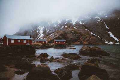 Stilt houses by sea against mountain during foggy weather