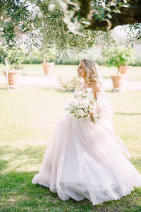 Full length of bride holding bouquet standing on grass