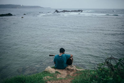 High angle view of man playing guitar while sitting on rock by sea