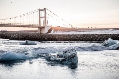 Bridge over frozen river against sky during winter