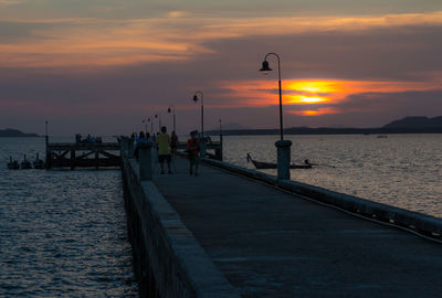 People on pier in sea against sky during sunset