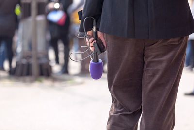 Midsection of person holding microphone while standing outdoors