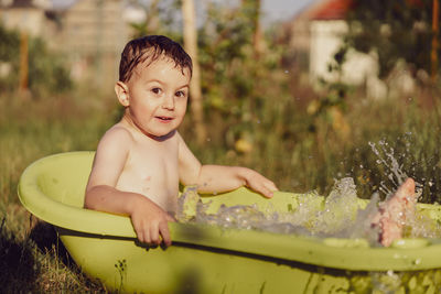 Cute little boy bathing in tub outdoors in garden. happy child is splashing, playing with water