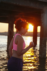 Side view of woman jogging by sea during sunset