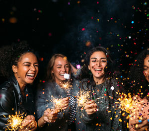 Cheerful female friends with burning sparkler at night