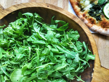 Close-up of arugula salad in bowl and fresh pizza on table