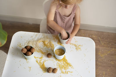 Toddler girl playing with grain, nuts, pasta and rice sitting at table.sensoric early development