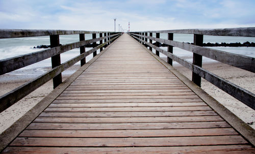 Wooden jetty leading to pier over sea against sky