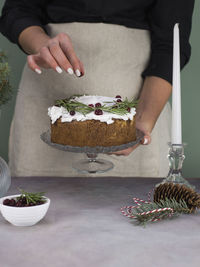 The girl's hands decorate the christmas cake with red berries on a gray table.