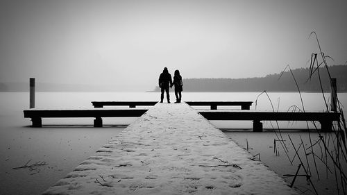 Rear view of silhouette friends standing by sea against sky