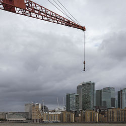 Low angle view of crane by buildings against sky