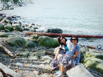 Portrait of young couple sitting on rock by sea