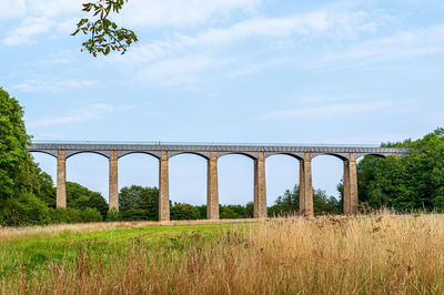 Arch bridge on field against sky