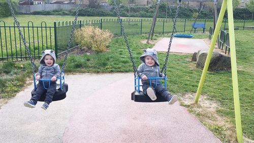 Portrait of cute boys sitting in swing at playground