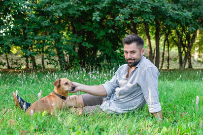 Handsome smiling man sitting on grass with his dog in park. concept of human and pet relationship.