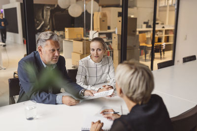 Mature businessman discussing with female colleagues at conference table in new office