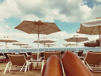 Low section of woman relaxing on chair at beach against sky