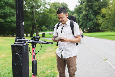 Man using smart phone standing near electric scooter at park