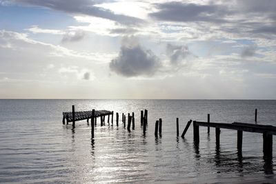 Wooden posts on jetty in sea against sky