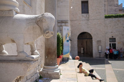 Statue by woman resting on steps in city