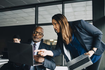 Businesswoman pointing on laptop while explaining to colleague in office