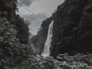 Low angle view of waterfall amidst rocks against sky