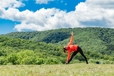 Rear view of woman with arms outstretched standing on field against sky