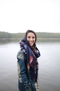 Portrait of smiling young woman standing against lake