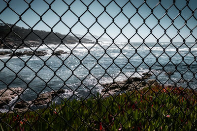 Scenic view of sea seen through chainlink fence