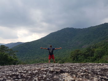 Rear view of man with arms outstretched standing against mountains