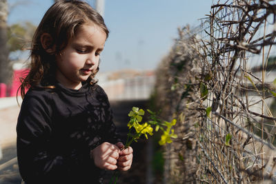 Adorable four-year-old girl looking at the yellow flowers in her hand.