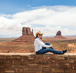 Woman sitting on rock against sky