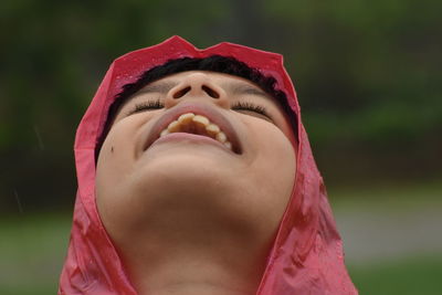 Close-up portrait of a smiling boy trying to enjoy rain