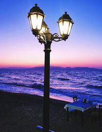 Street light by sea against sky during sunset