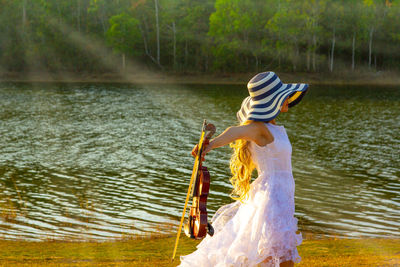 Side view of mature woman holding violin while standing by lake