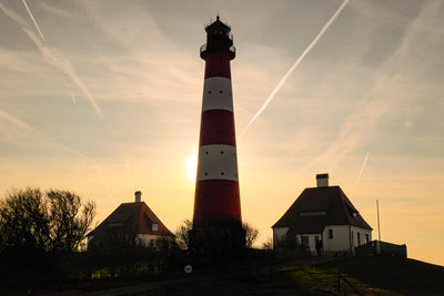 Lighthouse by building against sky during sunset