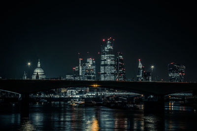 Illuminated buildings by river against sky at night