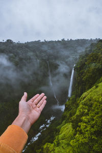 Cropped image of hand against waterfall
