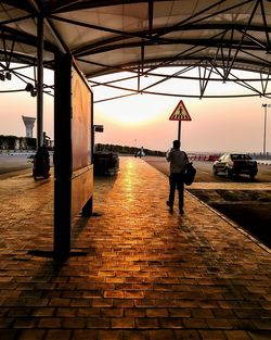 Rear view of silhouette man standing on sidewalk in city during sunset