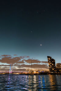 Illuminated city by sea against sky at night
