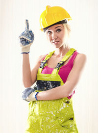 Portrait of female worker in coverall pointing while standing against wall