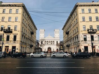 Cars on city street by buildings against sky