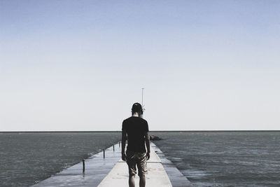 Rear view of man walking on sea against clear sky