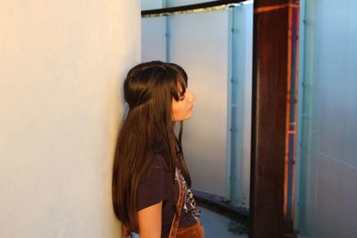 Side view of young woman standing by wall