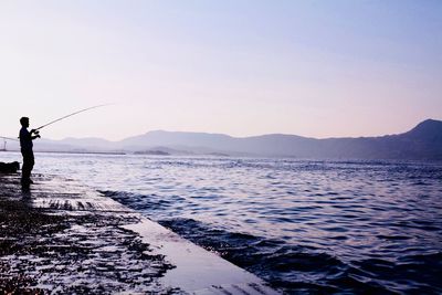 Man fishing in sea against clear sky