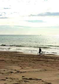 Man with bicycle on beach against sky